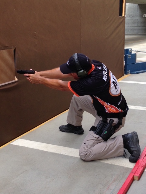 American Firearms Training instructor kneeling and aiming a handgun from cover